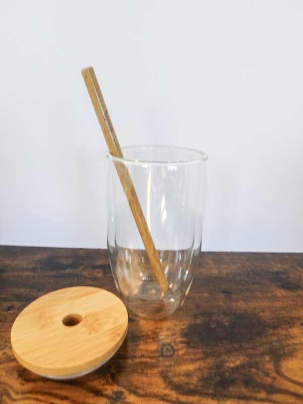 A glass with a straw and a wooden disk on the table.