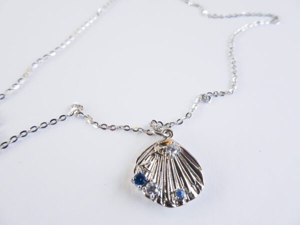 A silver necklace with a shell and blue stones.