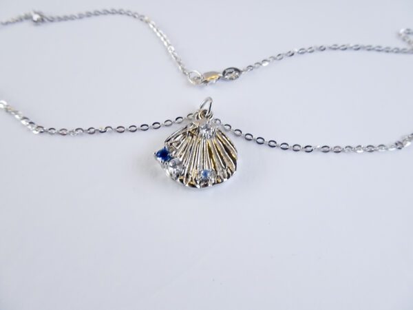 A silver necklace with a shell and blue stone.