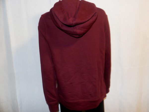 A person wearing a red hoodie standing next to a wall.