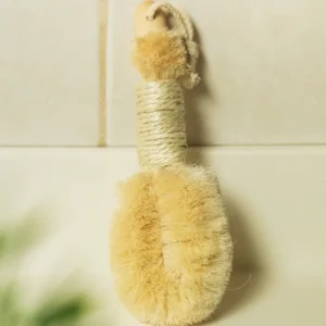 A brush hanging on the wall in front of a white tile.